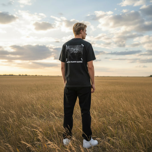Person wearing a black t-shirt with a graphic design standing in a field at sunset.