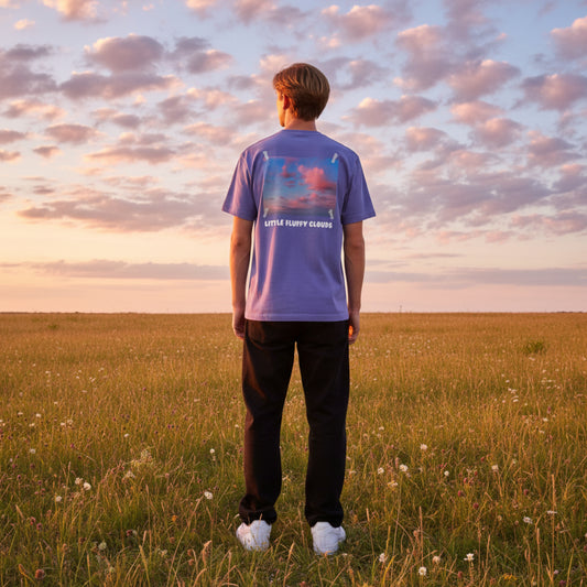 Purple t-shirt with a graphic of clouds and 'Little Fluffy Clouds' text on a male model standing in a field