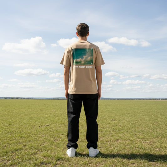 Beige t-shirt with a graphic of clouds and 'Little Fluffy Clouds' text on male model in a field
