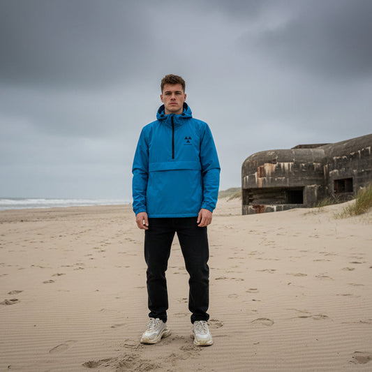 Man in a blue jacket standing on a beach with a bunker in the background