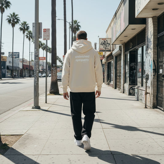 Beige hoodie with 'unfinished sympathy' text on the back on male model in LA