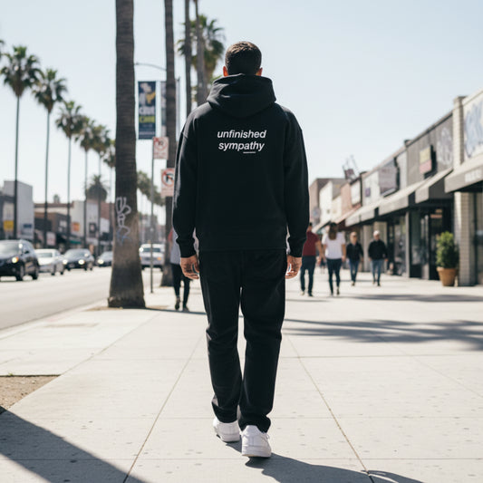 Black hoodie with 'unfinished sympathy' text on the back on male model in LA