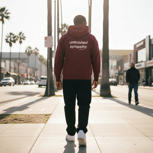Maroon hoodie with 'unfinished sympathy' text on the back on male model in LA