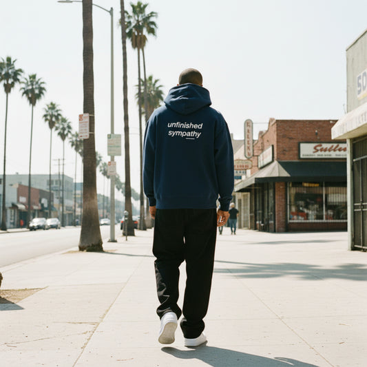 Navy blue hoodie with 'unfinished sympathy' text on the back on male model in LA