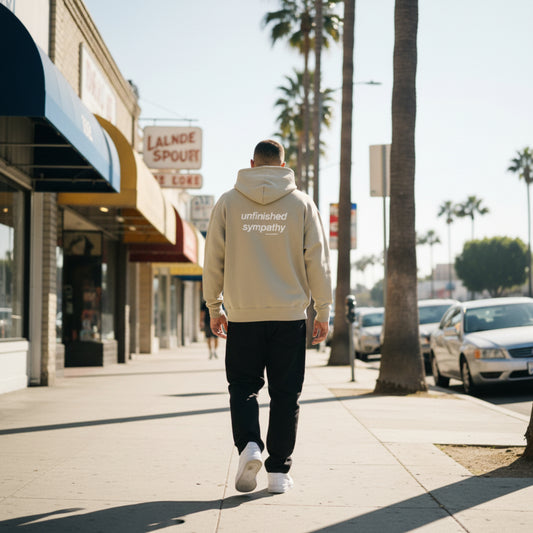 Beige hoodie with 'unfinished sympathy' text on the back on male model in LA
