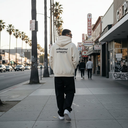 Beige hoodie with 'unfinished sympathy' text on the back on male model in LA