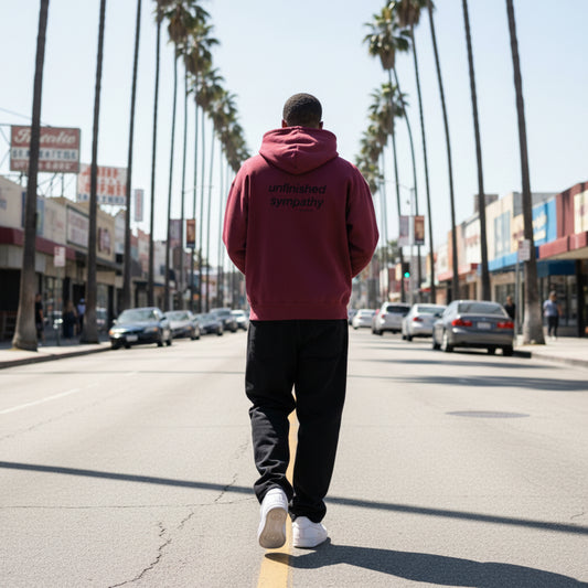 Burgundy hoodie with 'unfinished sympathy' text on the back on male model in LA