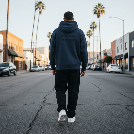 Navy blue hoodie with 'unfinished sympathy' text on the back on male model in LA