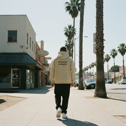 Clay hoodie with 'unfinished sympathy' text on the back on male model in LA