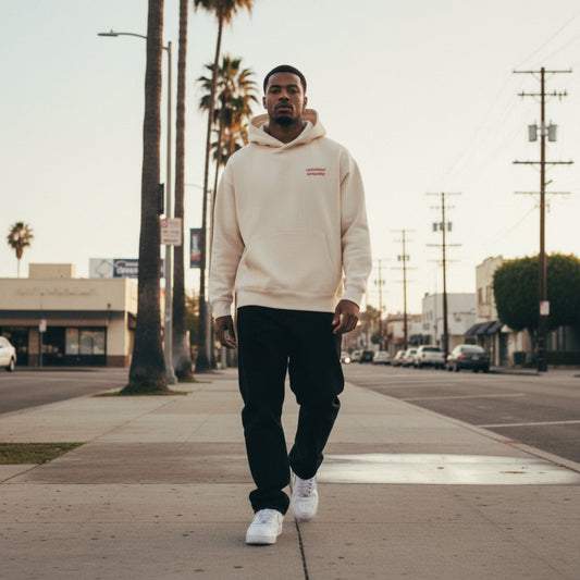 Beige hoodie with brick red 'unfinished sympathy' text on chest on male model in LA