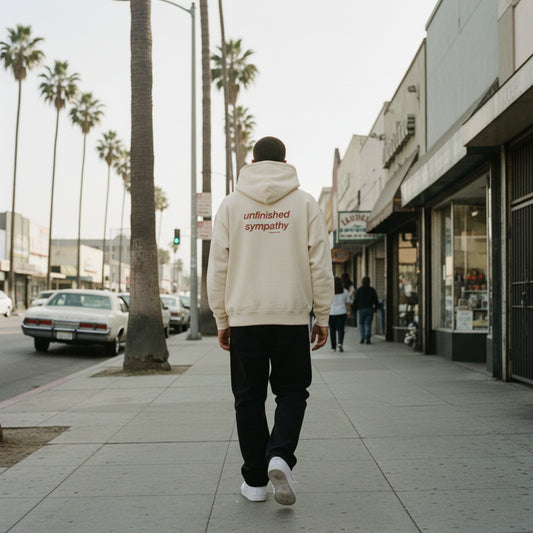 Beige hoodie with 'unfinished sympathy' text on the back on male model in LA