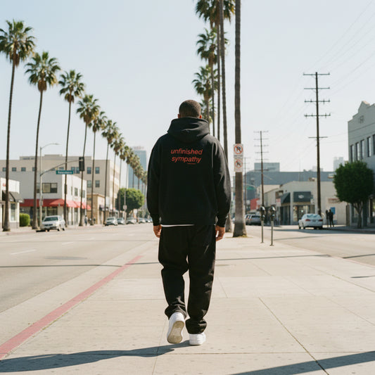 Black hoodie with 'unfinished sympathy' text on the back on male model in LA