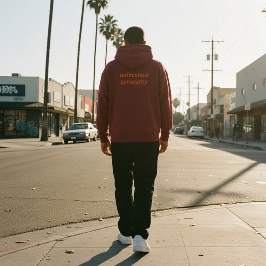 burgundy hoodie with 'unfinished sympathy' text on the back on male model in LA