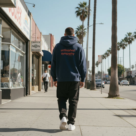 Navy blue hoodie with 'unfinished sympathy' text on the back on male model in LA