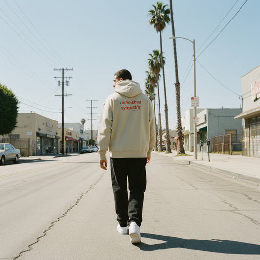 Beige hoodie with 'unfinished sympathy' text on the back on male model in LA